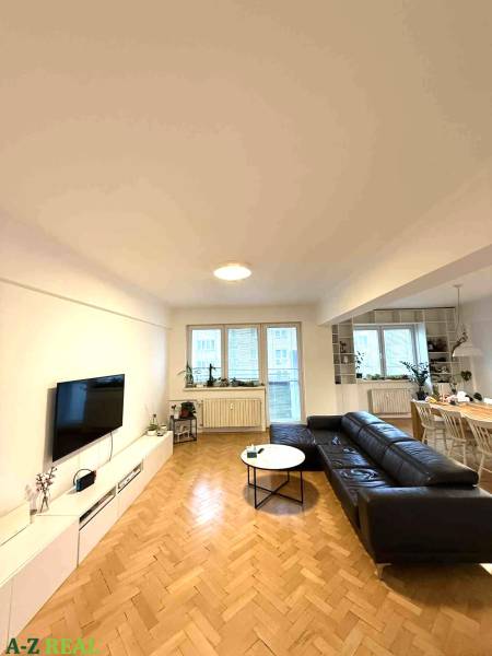 Prenájom 4 izb. bytu, Blumentálska ulica, Staré Mesto - Obývacia izba v 4-izbovom byte s podlahou s dreveným dekorom a čiernou sedačkou.