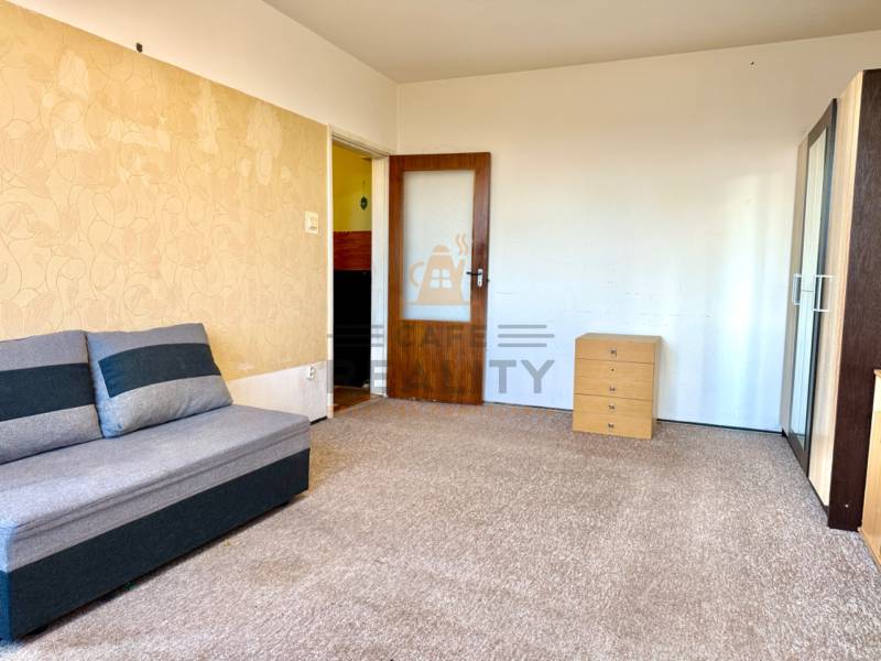 REZERVOVANÉ Na predaj 1 izbový byt, Bratislava, Dúbravka, Drobného - Izba s kobercovým pokrytím, sedačkou a skriňou v 1-izbovom byte.