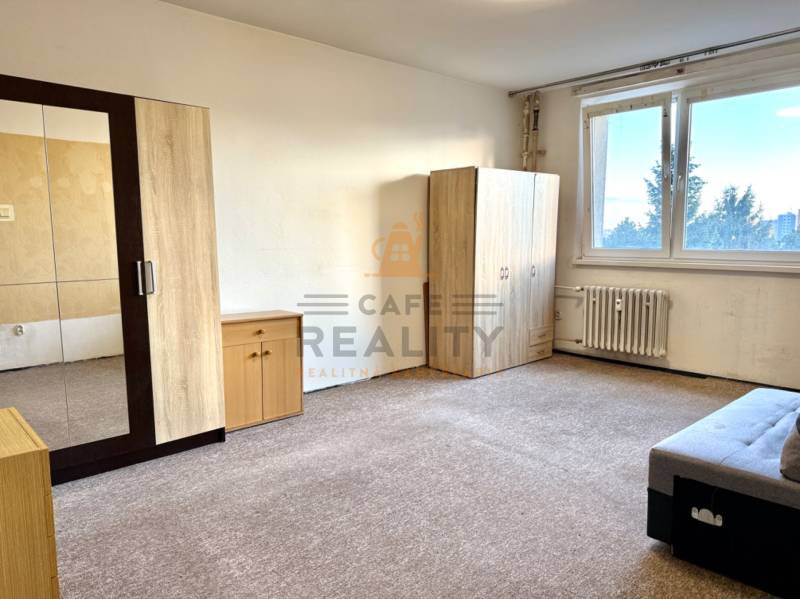 REZERVOVANÉ Na predaj 1 izbový byt, Bratislava, Dúbravka, Drobného - Izba v 1-izbovom byte s nábytkom a kobercom, svetlé steny, veľké okno.