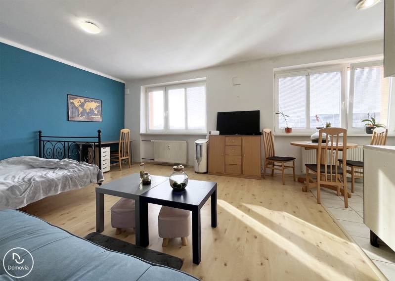 Exkluzívne | Na prenájom priestranný 1i byt Ružinove - 1-izbový byt s podlahou s dreveným dekorom, konferenčným stolom a modrou stenou.