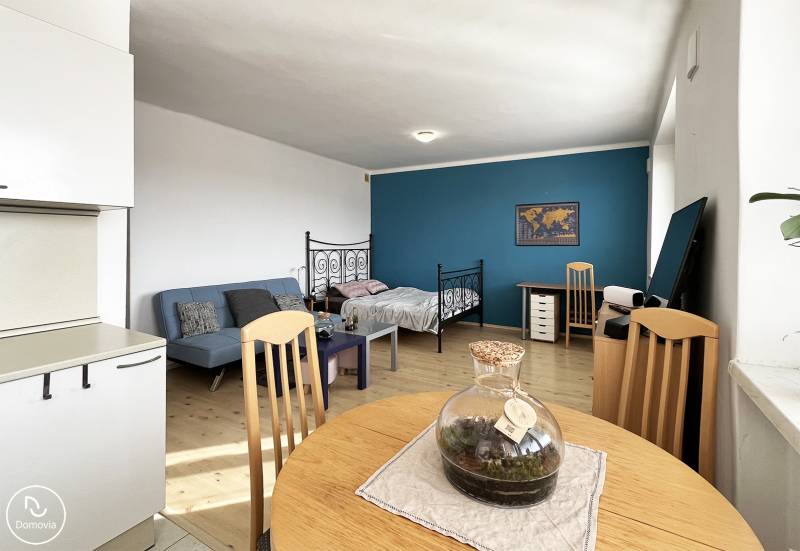 Exkluzívne | Na prenájom priestranný 1i byt Ružinove - Interiér 1-izbového bytu s podlahou s dreveným dekorom, pohovkou a pracovným stolom.