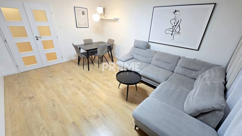 Moderný, rekonštruovaný 3i byt, pivnica, Jašíkova ul., Ružinov - Pošeň - Obývačka 3-izbového bytu so šedou sedačkou, jedálenským stolom a podlahou s dreveným dekorom.