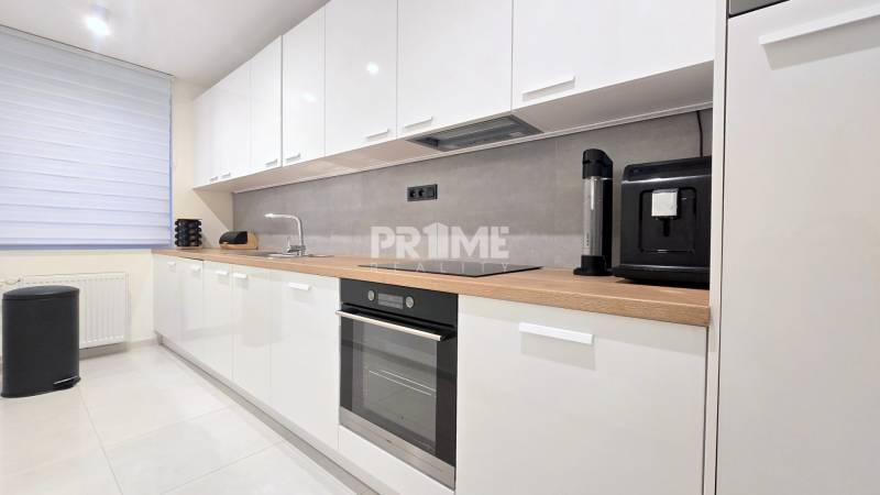 Moderný, rekonštruovaný 3i byt, pivnica, Jašíkova ul., Ružinov - Pošeň - Kuchyňa v 3-izbovom byte s bielymi skrinkami, spotrebičmi a pultom s dreveným dekorom.