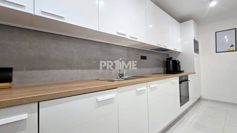 Moderný, rekonštruovaný 3i byt, pivnica, Jašíkova ul., Ružinov - Pošeň - Kuchynská linka v 3-izbovom byte s bielymi skrinkami a dreveným dekorom.