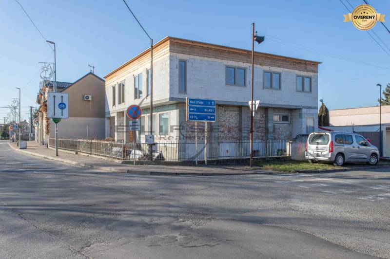 NA PREDAJ polyfunkčná budova v centre obce Veľké Leváre - Budova vo Veľkých Levároch, pri ceste, s parkovaným autom a dopravnými značkami.