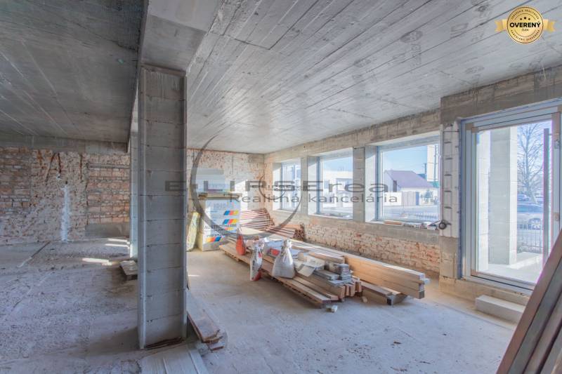 NA PREDAJ polyfunkčná budova v centre obce Veľké Leváre - Interiér budovy s tehlovými stenami, veľkými oknami a stavebným materiálom.