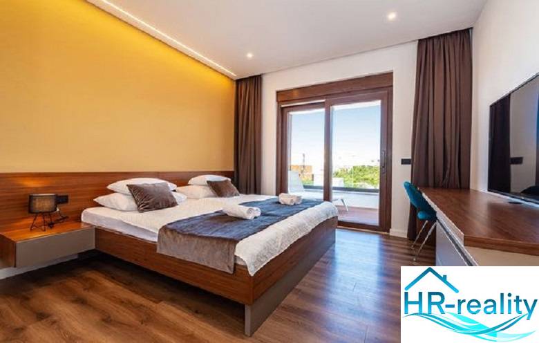 Novalja – luxusná vila s bazénom, jacuzzi a výhľadom na more - Elegantná spálňa vo vile s posteľou a podlahou s dreveným dekorom.