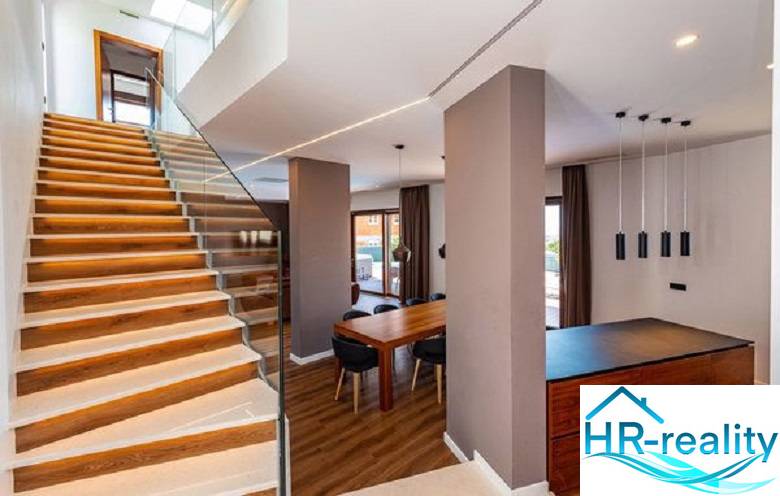 Novalja – luxusná vila s bazénom, jacuzzi a výhľadom na more - Interiér vily s drevenou podlahou, schodišťom a jedálenským stolom.