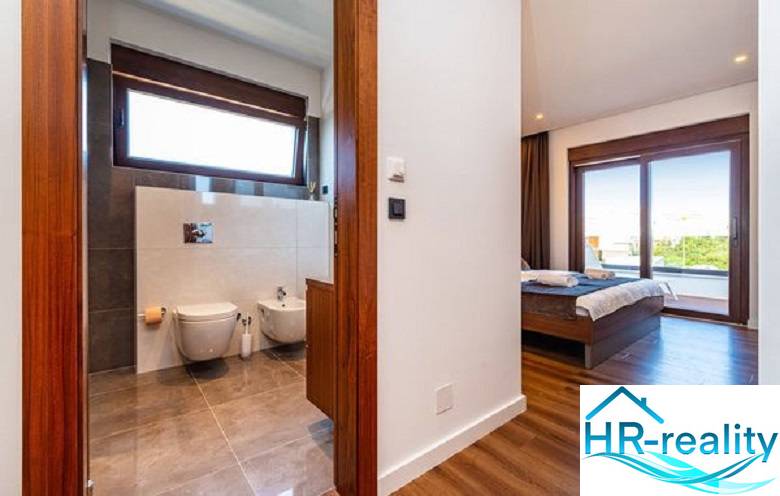 Novalja – luxusná vila s bazénom, jacuzzi a výhľadom na more - Interiér vily s podlahou s dreveným dekorom, spálňa a kúpeľňa s veľkým oknom.