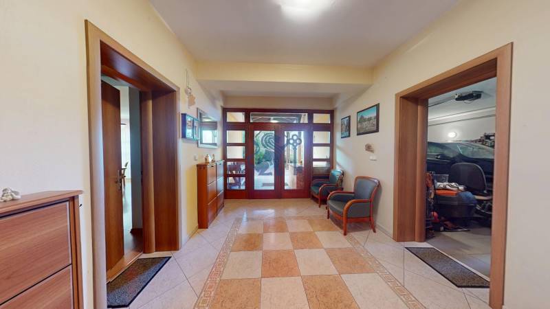 Veľkometrážny dom s wellness, bazénom a investičným potenciálom - Chodba v rodinnom dome s dlažbou a dreveným nábytkom, vedúca do garáže.