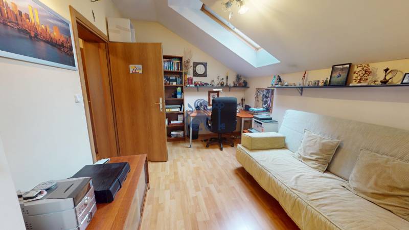 Veľkometrážny dom s wellness, bazénom a investičným potenciálom - Podkrovná izba v rodinnom dome s podlahou s dreveným dekorom, písacím stolom a sedačkou.