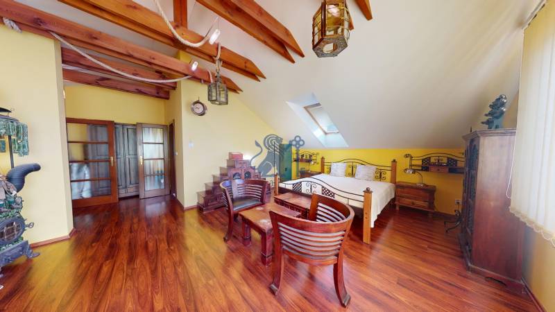 Veľkometrážny dom s wellness, bazénom a investičným potenciálom - Podkrovná izba s drevenými trámami, veľkou posteľou a podlahou s dreveným dekorom v rodinnom dome.