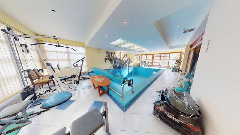 Veľkometrážny dom s wellness, bazénom a investičným potenciálom - Interiér rodinného domu s bazénom a posilňovacími strojmi, svetlé priestory s veľkými oknami.