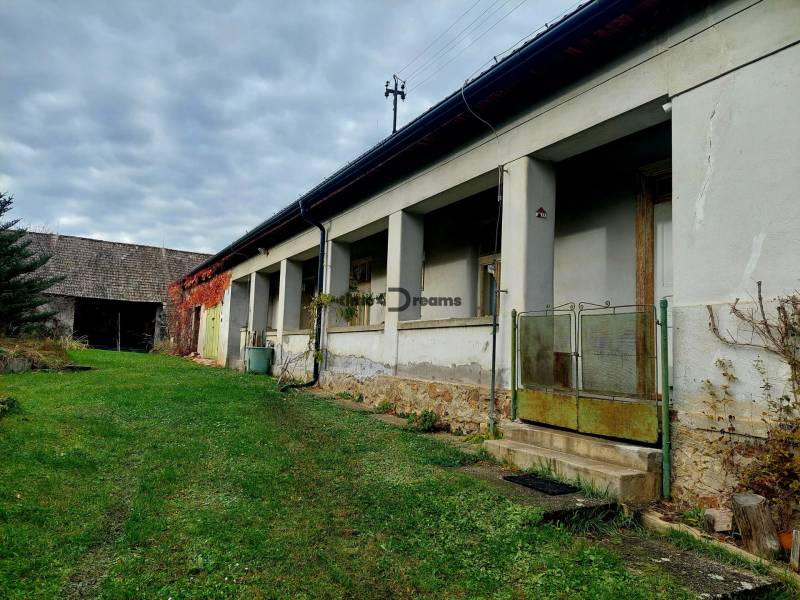 NA PREDAJ rodinný dom - Lehota nad Rimavicou - Rodinný dom s verandou a záhradou, obklopený zeleňou, pod zamračenou oblohou.