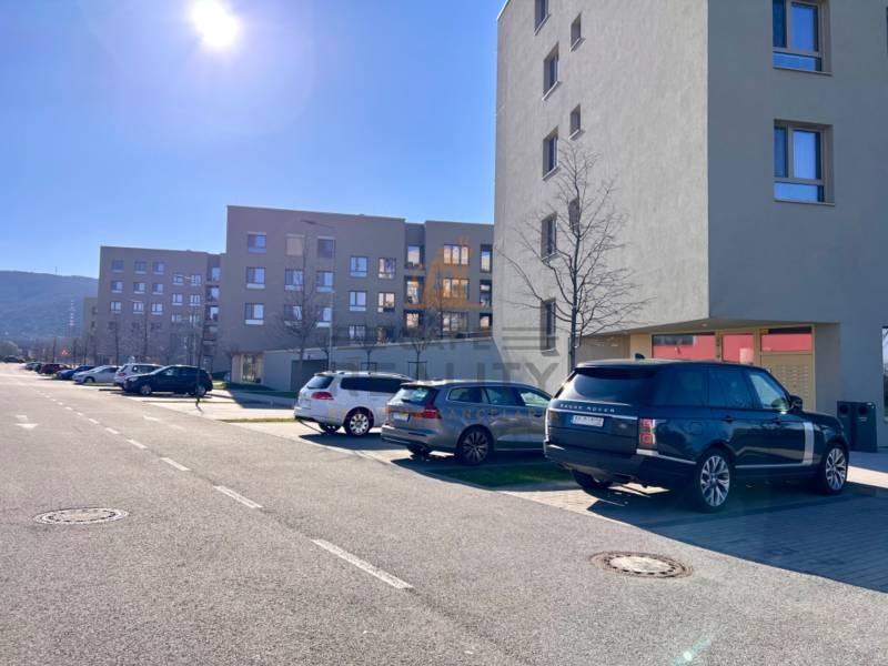 Na prenájom vonkajšie parkovacie státie Bratislava, BORY, Kolakoviča - Autá zaparkované na ulici Tomislava P. Kolakoviča, garáže pri bytovke, slnečný deň.