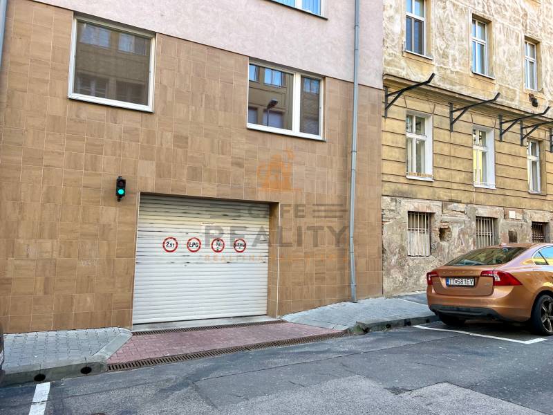 Na predaj parkovacie miesto, Beskydská, Bratislava, Staré Mesto - Brána v centre mesta s dopravnými značkami a hnedým autom, garáže v pozadí.