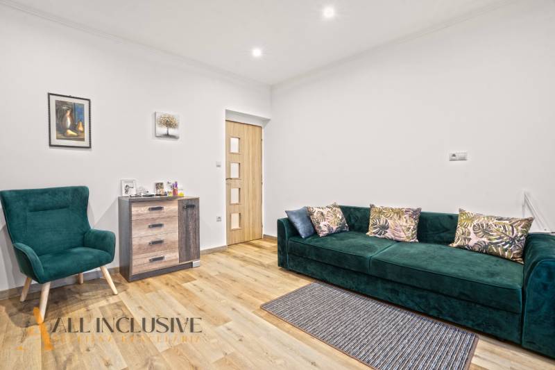 NA PREDAJ 4-IZBOVÝ RODINNÝ DOM V KOLÁROVE - Obývacia izba s podlahou s dreveným dekorom, zeleným kreslom a pohovkou v rodinnom dome.