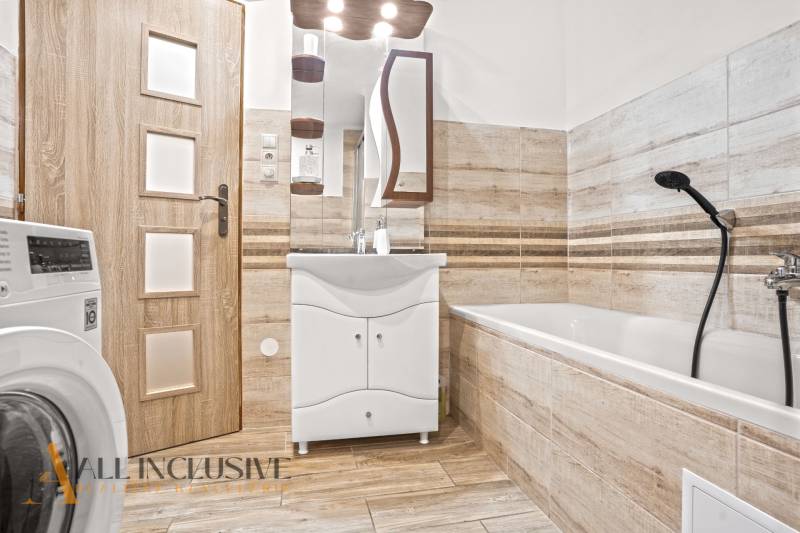 NA PREDAJ 4-IZBOVÝ RODINNÝ DOM V KOLÁROVE - Kúpeľňa v rodinnom dome s vaňou, podlahou s dreveným dekorom a práčkou.