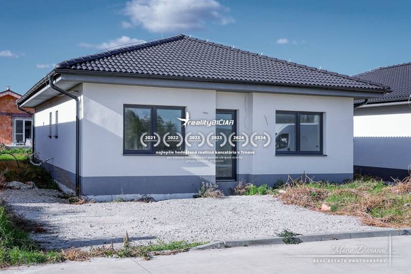 Novostavba 4-izbového rodinného domu v obci Slov.Nová Ves - Rodinný dom v Slovenskej Novej Vsi na ulici Slovenská Nová Ves s tmavou strechou a parkoviskom.