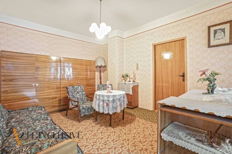 NA PREDAJ 3-IZBOVÝ RODINNÝ DOM VO VEĽKOM BLAHOVE - Obývacia izba v rodinnom dome s retro nábytkom, vzorovaným kobercom a záclonami.