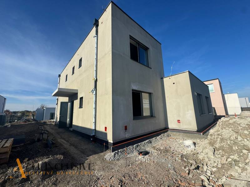 NA PREDAJ 4-IZB. POSCHODOVÝ RD (ČASŤ DVOJDOMU), HUBICE - Rodinný dom v Hubiciach vo výstavbe, s minimalistickým exteriérom a susednými budovami.