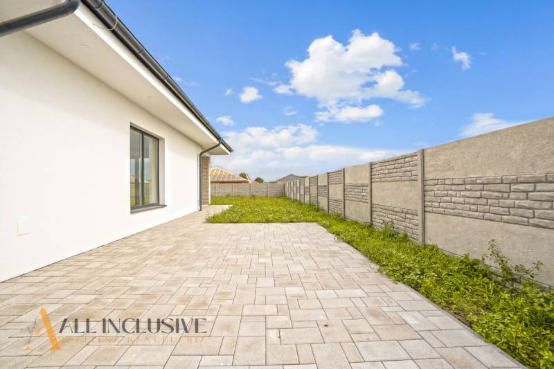 NA PREDAJ 4-IZBOVÁ NOVOSTAVBA, POVODA - Dvor rodinného domu na ulici Povoda v Dunajskej Strede s vydláždenou terasou a plotom.