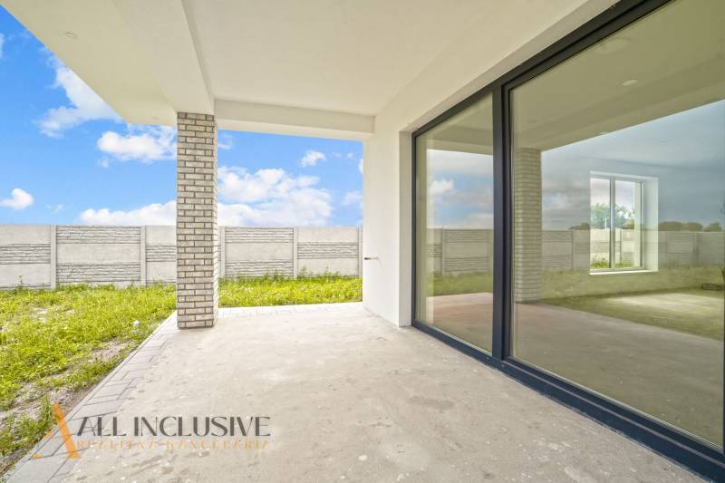 NA PREDAJ 4-IZBOVÁ NOVOSTAVBA, POVODA - Terasa rodinného domu v Dunajskej Strede na ulici Povoda s betónovou podlahou a veľkými oknami.