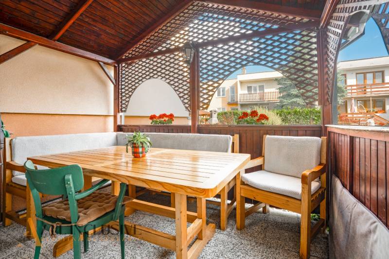 NA PREDAJ 5-IZBOVÝ POSCH. RODINNÝ DOM, DUNAJSKÁ STREDA - Terasa rodinného domu v Dunajskej Strede s dreveným sedením a kvetmi.