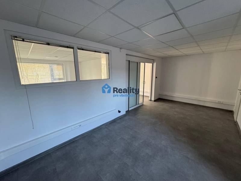 Prenájom obchod/kancelária NP nová kompletná rekonštrukcia, centrum PB - Obchodné priestory s presklenými dverami, šedou podlahou a podhľadovým stropom.