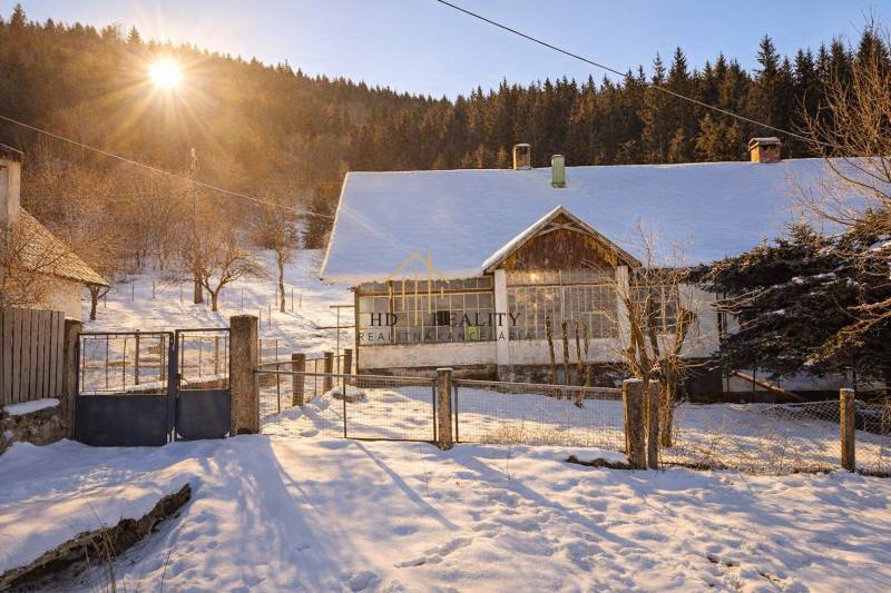 Predaj, rodinný dom Sliačany, Donovaly - Zasnežený rodinný dom v Donovaloch, obklopený stromami a zachytený pod zapadajúcim slnkom.