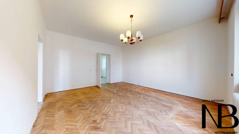 Na predaj 2,5 izbový byt v pôvodnom stave, 79 m2, Pod Sokolice, TN - Svetlá izba s podlahou s dreveným dekorom, luster visí v 2-izbovom byte.