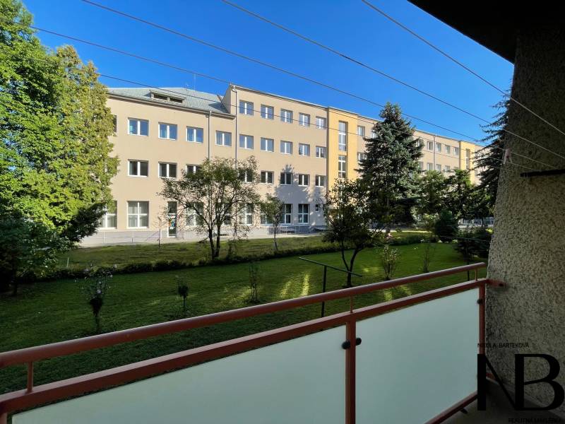 Na predaj 2,5 izbový byt v pôvodnom stave, 79 m2, Pod Sokolice, TN - Pohľad z balkóna 2-izbového bytu na ulici Pod Sokolice v Trenčíne na zeleň a budovu.