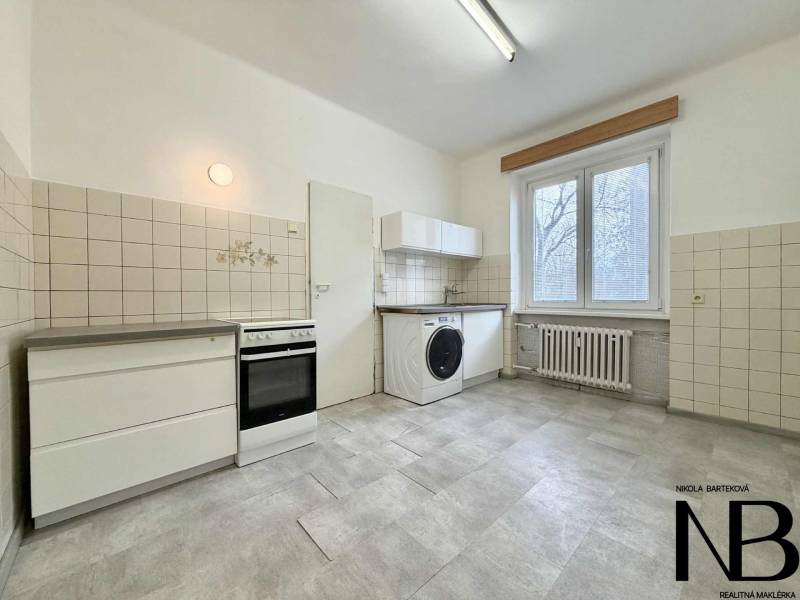 Na predaj 2,5 izbový byt v pôvodnom stave, 79 m2, Pod Sokolice, TN - Kuchyňa v 2-izbovom byte s bielymi dlaždicami, sporákom a práčkou.