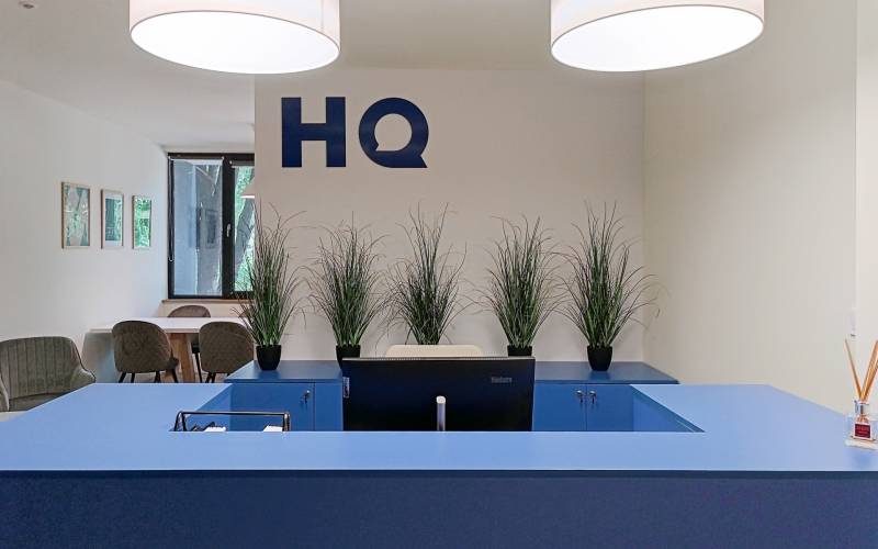 Neobmedzený prístup do coworkingu v oblasti HQ Seberiniho - Recepcia s modrým pultom, rastlinami a počítačom v Kanceláriách.