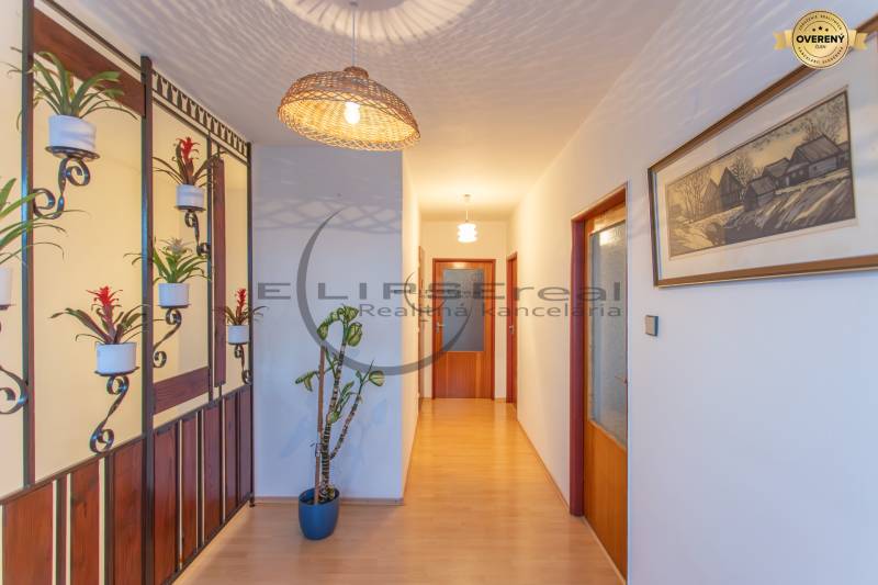 NA PREDAJ priestranný 4-izbový rodinný dom v Plaveckom Štvrtku - Chodba v rodinnom dome s podlahou s dreveným dekorom, kvetinami a osvetlením.