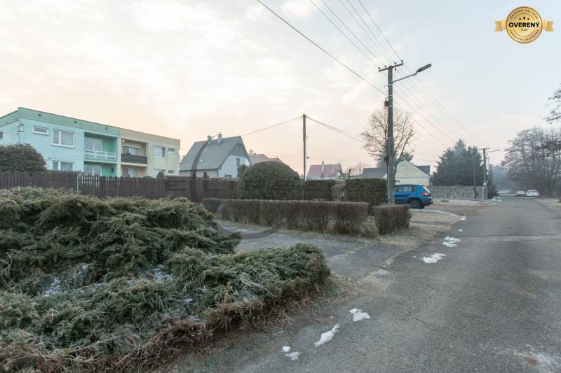 NA PREDAJ priestranný 4-izbový rodinný dom v Plaveckom Štvrtku - Ulica v Plaveckom Štvrtku so zástavbou rodinných domov, parkovacími miestami a elektrickými stĺpmi.