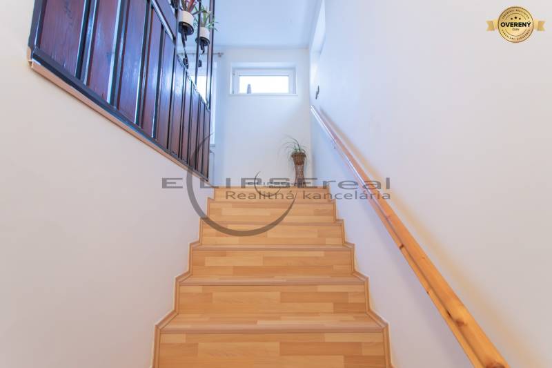NA PREDAJ priestranný 4-izbový rodinný dom v Plaveckom Štvrtku - Schodisko so zábradlím, podlaha s dreveným dekorom, biele steny, črepník.
