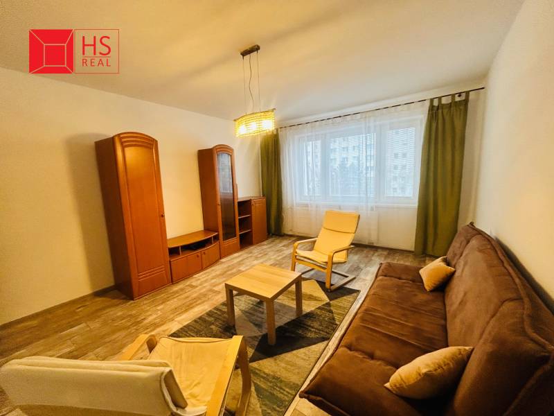 Prenajom 3 izb. bytu na Vajanskeho v NZ - Obývacia izba v 3-izbovom byte s hnedou sedačkou a podlahou s dreveným dekorom.