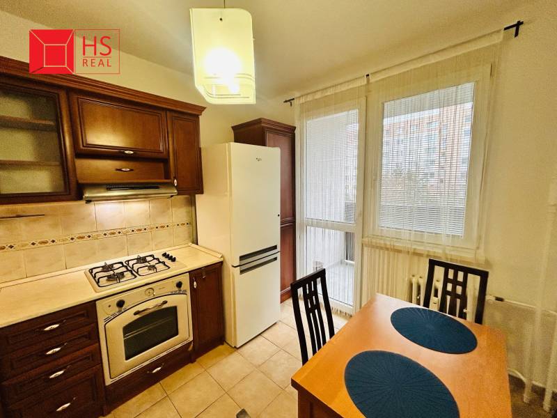 Prenajom 3 izb. bytu na Vajanskeho v NZ - Kuchyňa v 3-izbovom byte s drevenými skrinkami a jedálenským stolom s dvoma stoličkami.