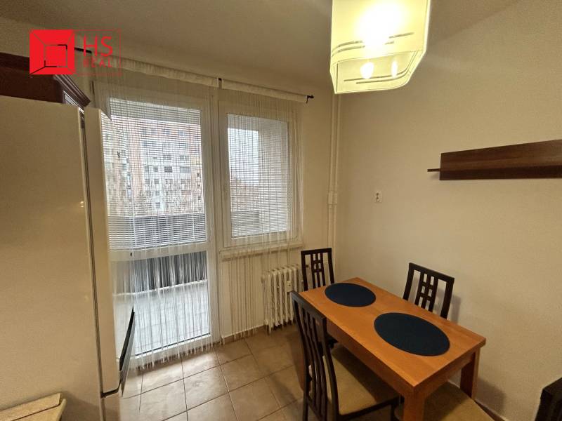 Prenajom 3 izb. bytu na Vajanskeho v NZ - Kuchyňa so stolom a stoličkami v 3-izbovom byte, dlažba na podlahe, výhľad cez okno.