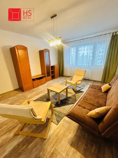 Prenajom 3 izb. bytu na Vajanskeho v NZ - Obývacia izba v 3-izbovom byte s podlahou s dreveným dekorom, pohodlným sedením a nábytkom.