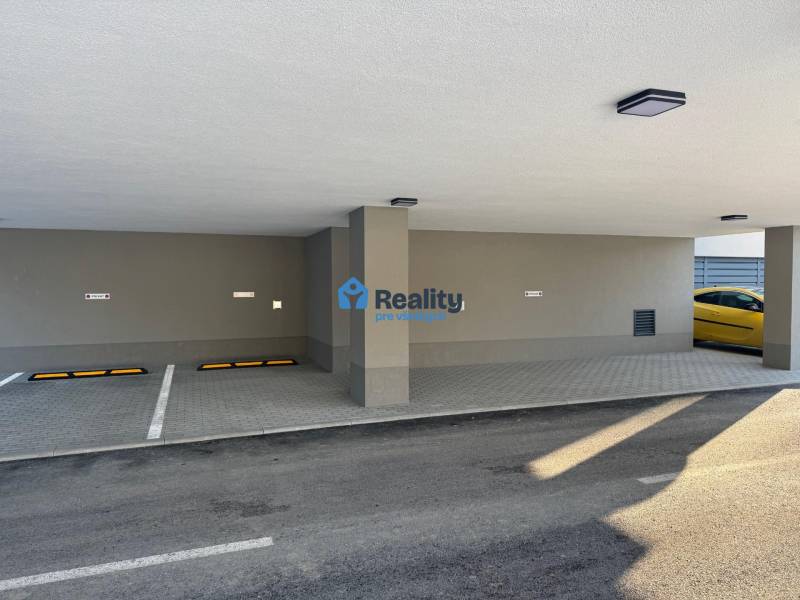 Nájom parkovacie miesto-kryté, centrum PB - Parkovacie garáže v Považskej Bystrici s dvomi voľnými miestami a žltým autom.