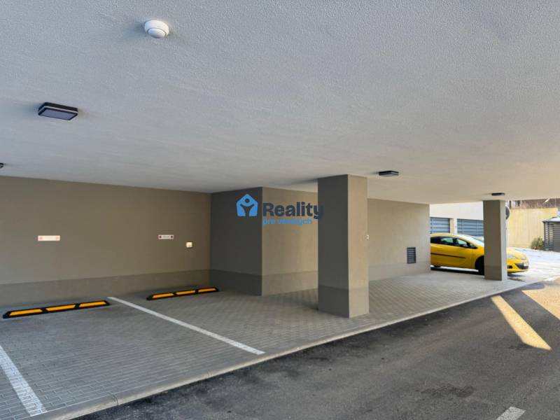 Nájom parkovacie miesto-kryté, centrum PB - Považská Bystrica: Garáže s parkovacími miestami a žltým vozidlom, stĺpy, dlažba, strop svetlá.