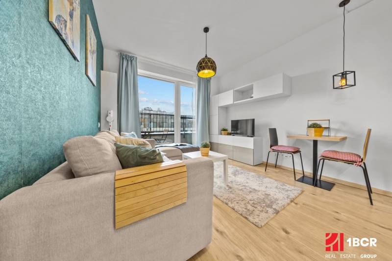 ZARIADENÝ 1-IZBOVÝ BYT, SLNEČNICE – IDEÁLNA INVESTÍCIA AJ BÝVANIE - Svetlá obývačka s pohovkou, jedálenským stolom a podlahou s dreveným dekorom v 1-izbovom byte.