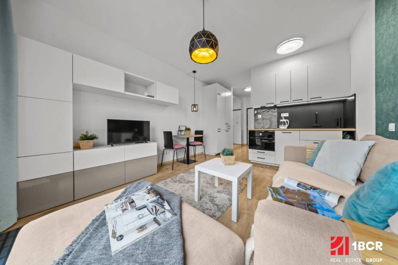 ZARIADENÝ 1-IZBOVÝ BYT, SLNEČNICE – IDEÁLNA INVESTÍCIA AJ BÝVANIE - 1-izbový byt so svetlou nábytkom, podlahou s dreveným dekorom a obývacou stenou.