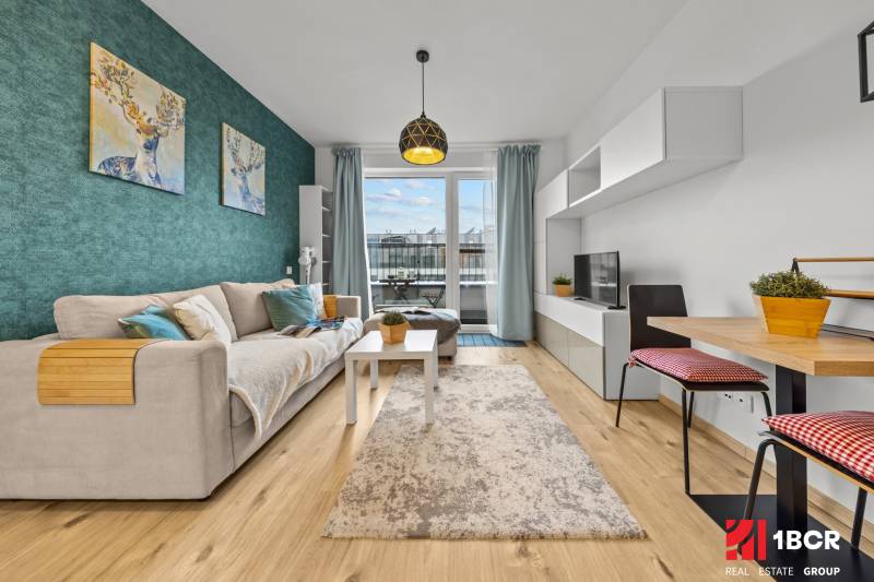 ZARIADENÝ 1-IZBOVÝ BYT, SLNEČNICE – IDEÁLNA INVESTÍCIA AJ BÝVANIE - Obývacia izba v 1-izbovom byte s pohovkou, TV, kobercom a podlahou s dreveným dekorom.