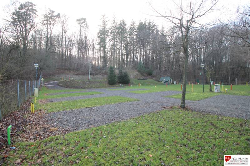 Zabehnutý multifunkčný rekreačný areál (kemp) Kuchyňa na predaj - Rekreačné pozemky v Kuchyni s trávnikmi a lesnou krajinou v pozadí.