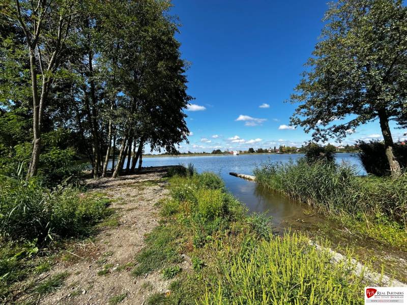 Zabehnutý multifunkčný rekreačný areál (kemp) Kuchyňa na predaj - Rekreačné pozemky pri jazere obklopené stromami a trávou v Kuchyni.