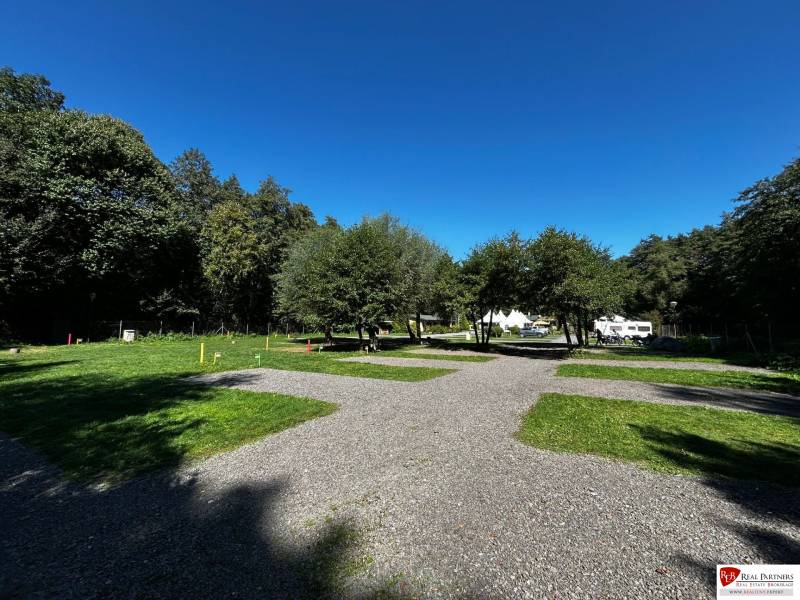 Zabehnutý multifunkčný rekreačný areál (kemp) Kuchyňa na predaj - Rekreačné pozemky v Kuchyni s karavanmi obklopené stromami a modrou oblohou.