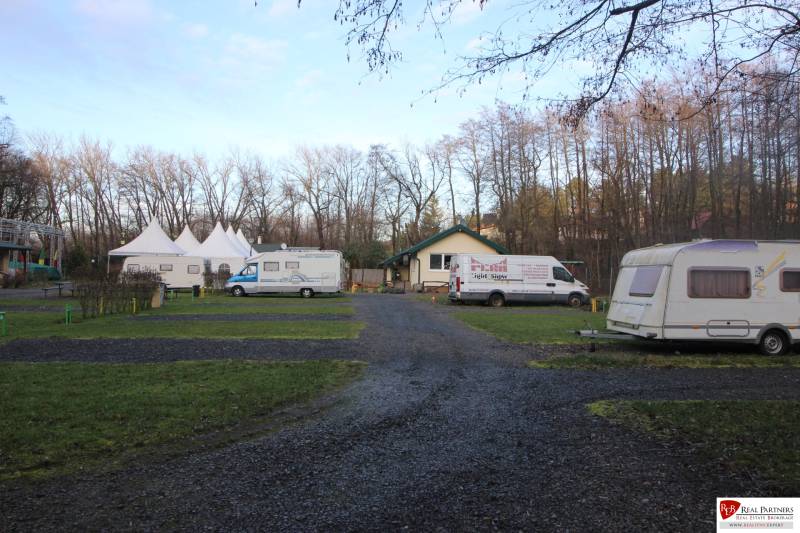 Zabehnutý multifunkčný rekreačný areál (kemp) Kuchyňa na predaj - Karavany a stany na rekreačných pozemkoch v Kuchyni obklopené stromami.